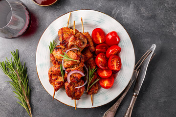 Pork kebab with barbecue sauce and tomatoes and a glass of red wine on a grey background top view close up
