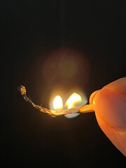 Close-up of a burnt matchstick held by fingers with glowing flame in the dark. Symbol of burnout,...