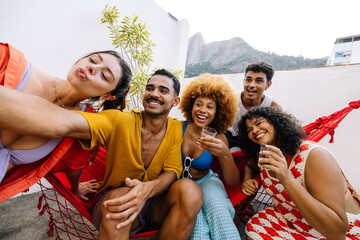 Brazilian friends taking a fun rooftop selfie with drinks on a summer day