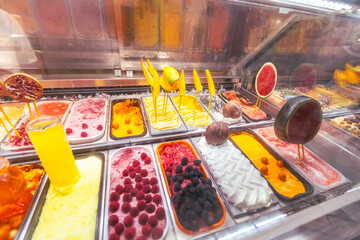 Close-up view of professional gelato counter showing various ice cream flavors decorated with fresh...