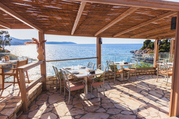 Stunning seaside restaurant terrace featuring natural bamboo pergola ceiling, stone dining tables with elegant place settings, and breathtaking panoramic ocean views of Mediterranean coastline.