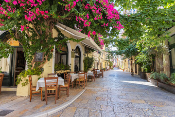 Fototapeta premium Picturesque Mediterranean street lined with vibrant bougainvillea flowers, outdoor dining tables, and charming architecture. Scene captures the essence of a lively yet peaceful coastal town. Corfu.
