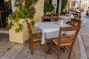 Serene outdoor dining setup featuring wooden chairs, white tablecloths, and a textured stone wall adorned with greenery. The scene exudes a cozy, rustic ambiance perfect for leisurely meals.