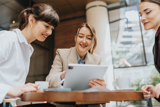 Three women sharing ideas outdoors, fostering teamwork and collaboration using digital technology.