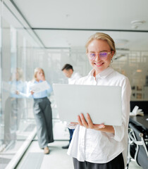 In a modern office, a young professional smiles while using a tablet, enjoying teamwork and...
