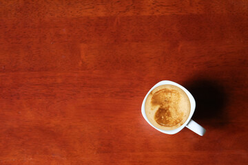 A white cup of hot coffee with milk foam on a wooden surface, placed with empty copy space for text...