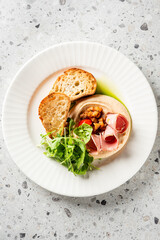 Gourmet appetizer with toasted bread, hummus, cured meat, microgreens, and herb oil, elegantly plated on a white dish for fine dining presentation
