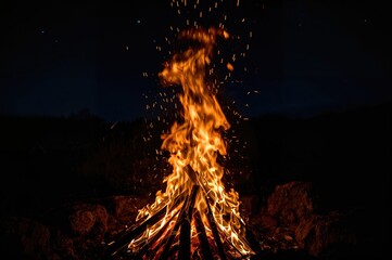 An open-air campfire with flickering orange flames lighting up the dark evening