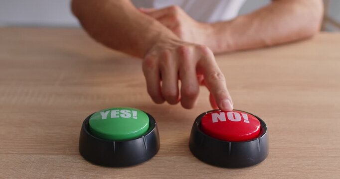 Closeup of a hand about to press a red NO button next to a green YES button on a wooden table, symbolizing choice, decision, and vote with a game buzzer feel. A hand chooses the no option.