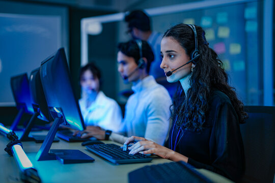 A diverse team of professionals works at a customer support call center. A female operator in a headset assists a client, providing excellent 24/7 technical or sales service. - Powered by Adobe