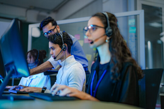 A diverse team of professionals works at a customer support call center. A female operator in a headset assists a client, providing excellent 24/7 technical or sales service.