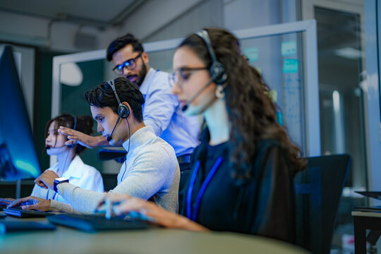 A diverse team of customer service agents wearing headsets works in a modern call center. Professional operators provide technical support and assistance to clients day and night. - Powered by Adobe