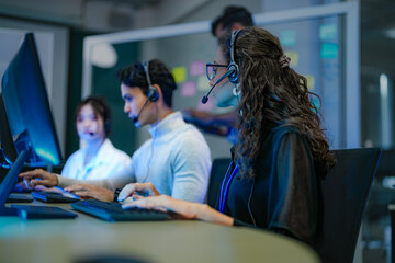 A diverse team of customer service agents wearing headsets works in a modern call center....