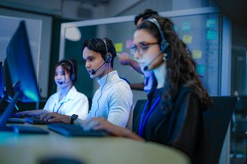 A diverse team of customer service agents wearing headsets works in a modern call center....