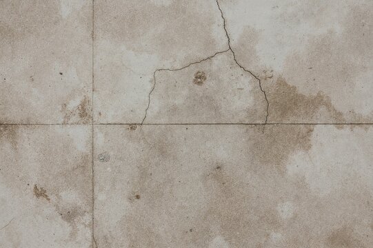 Close-up view of a textured stone surface with rectangular shapes, cracks, and stains showing signs of aging