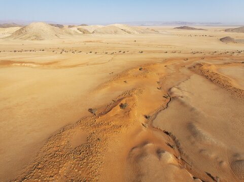 Arid plains grown with camelthorn trees (Vachellia erioloba), sand dunes and bare mountain ridges in the Tsondab Valley in the Namib Desert. Aerial view. Drone shot. Namibia