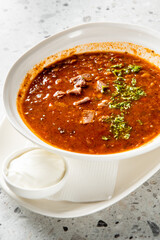 Traditional beef soup served in a white bowl with sour cream and herbs on a rustic stone background. Classic Eastern European comfort food presentation