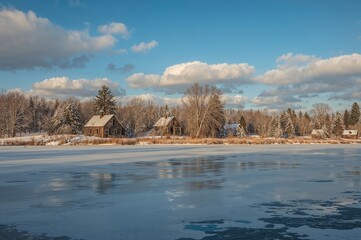 Close-up of icy lake featuring remnants of old buildings, winter scenery with trees and sky