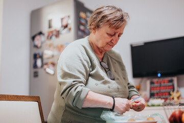 A focused elderly woman peels vegetables in a cozy kitchen environment, showcasing homeliness,...