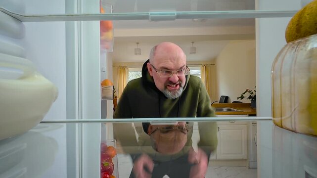Man opening fridge and yelling impulsively in anger at empty shelves, view from inside of fridge. Male reacting to lack of food while feeling furious and desperate. Guy screaming with frustration and