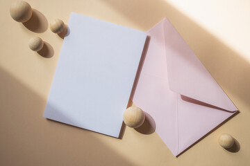 Empty white blank greeting or invitation card with pink envelope on beige background. Mock up presentation.