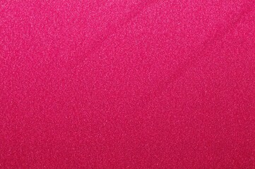 Shiny sparkling pink and red wrapping paper texture on magenta fabric backdrop for festive and wedding invitation design elements