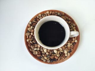 A cup of coffee inside the coffee beans on a wooden plate. Flat lay composition on a white background.
