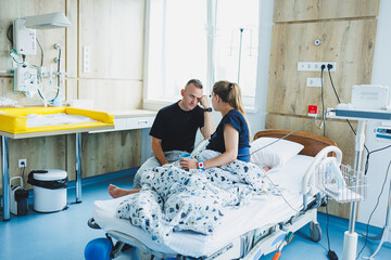 A woman lies in the delivery room during labor and her husband holds her hand. The couple gives birth together. Husband supports her during labor. The woman gives birth and it hurts a lot.