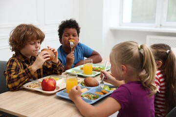 Little kids eating lunch at wooden table in school canteen