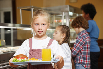 Little girl with tray of tasty food in school canteen, selective focus