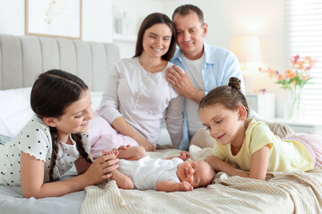 Parents watching their older daughters admiring newborn baby on bed at home, selective focus