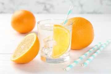 Sparkling water with orange slice in glass and fresh fruits on white wooden table, closeup