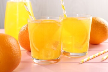 Refreshing soda water with orange slices in glasses, jug and fresh fruits on pink wooden table,...