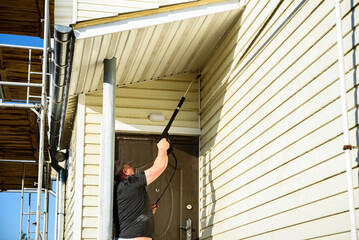 Cleaning the vinyl siding wall with a high-pressure washer.