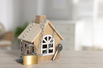 Home security. House model with chain, key and padlock on wooden table indoors, closeup. Space for...