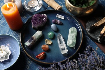 Chakra gemstones, lavender flowers, incense and burning candles on blue wooden table, closeup