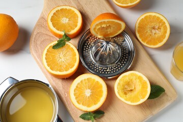 Squeezer with oranges, mint and fresh juice on white table, flat lay