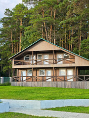 Wooden cabin by pine forest, eco lodge with balconies and green lawn