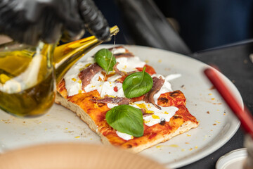 A slice of pizza topped with fresh basil leaves, anchovies, and stracciatella. The pizza is served...