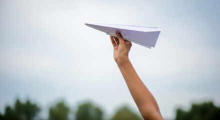 A person holding a white paper airplane up to the sky in outdoor setting