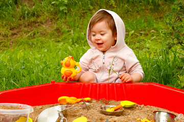 happy baby plays with toys in the sandbox on the playground