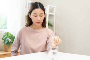 Smile asian young woman putting or dropping effervescent tablet into glass of water, holding pain...