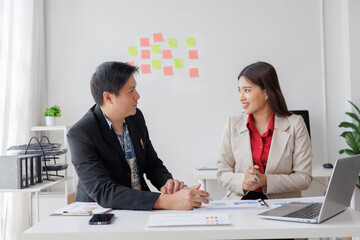 Asian businesspeople discussing strategy during a meeting in the office, analyzing financial charts and using laptop