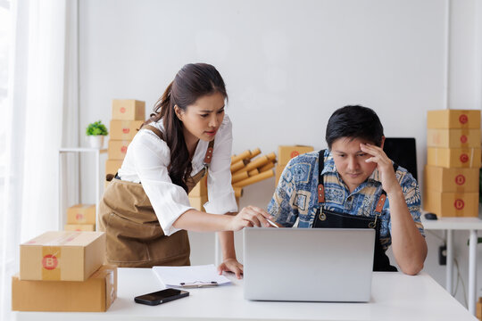 Two worried entrepreneurs analyzing data on a laptop, surrounded by cardboard boxes, possibly facing a challenge in their online business