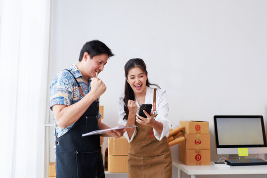 Asian entrepreneurs expressing joy and excitement while checking online sales or financial reports