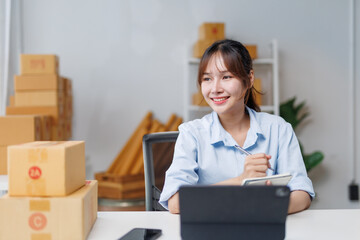 Young asian woman entrepreneur taking notes while working in her home office managing her online...