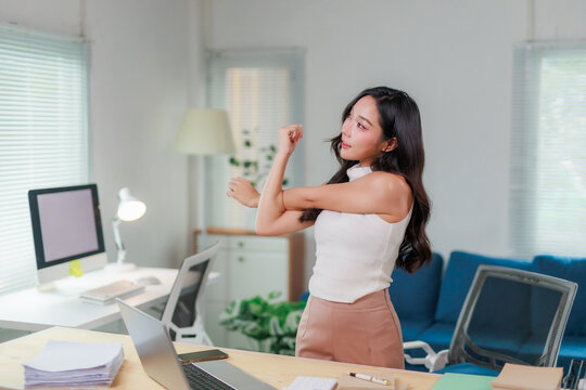 Businesswoman stretching arms while working on computer at office desk, taking a break from work to refresh and relieve stress