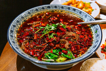 Traditional Sichuan boiled beef in spicy red broth with chili peppers and greens, garnished with cilantro and served in a patterned ceramic bowl