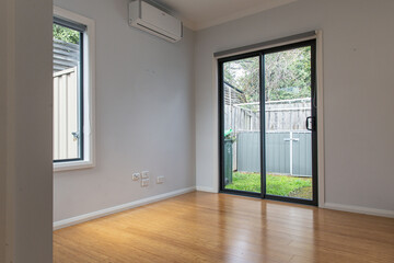Minimalist modern interior with bamboo flooring, light gray walls, and a glass sliding door opening to a small fenced backyard with green grass