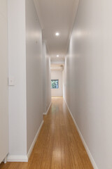 Long interior hallway of a modern home with bamboo flooring, clean white walls, and soft overhead lighting leading to a bright window at the end